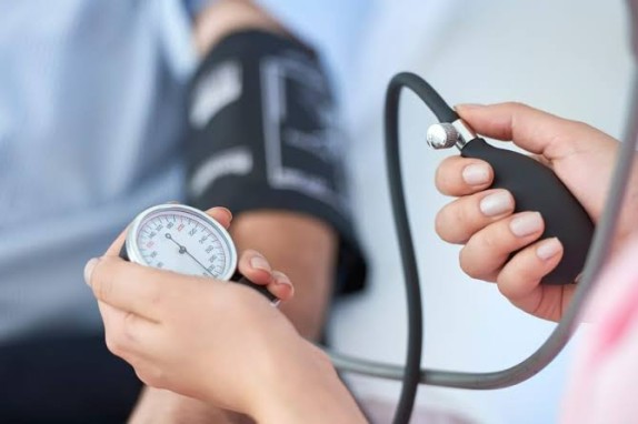 Close-up of a clinician inflating a blood pressure cuff on a patient's upper arm, with a sphygmomanometer gauge visible.