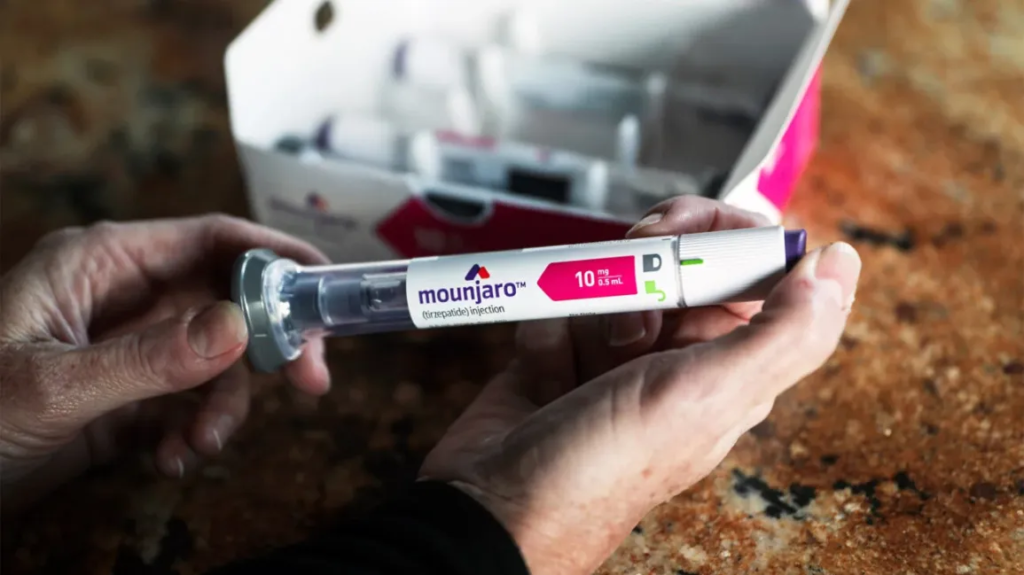 Close-up of hands holding a Mounjaro tirzepatide injection pen, dose window visible, ready for use on a kitchen countertop